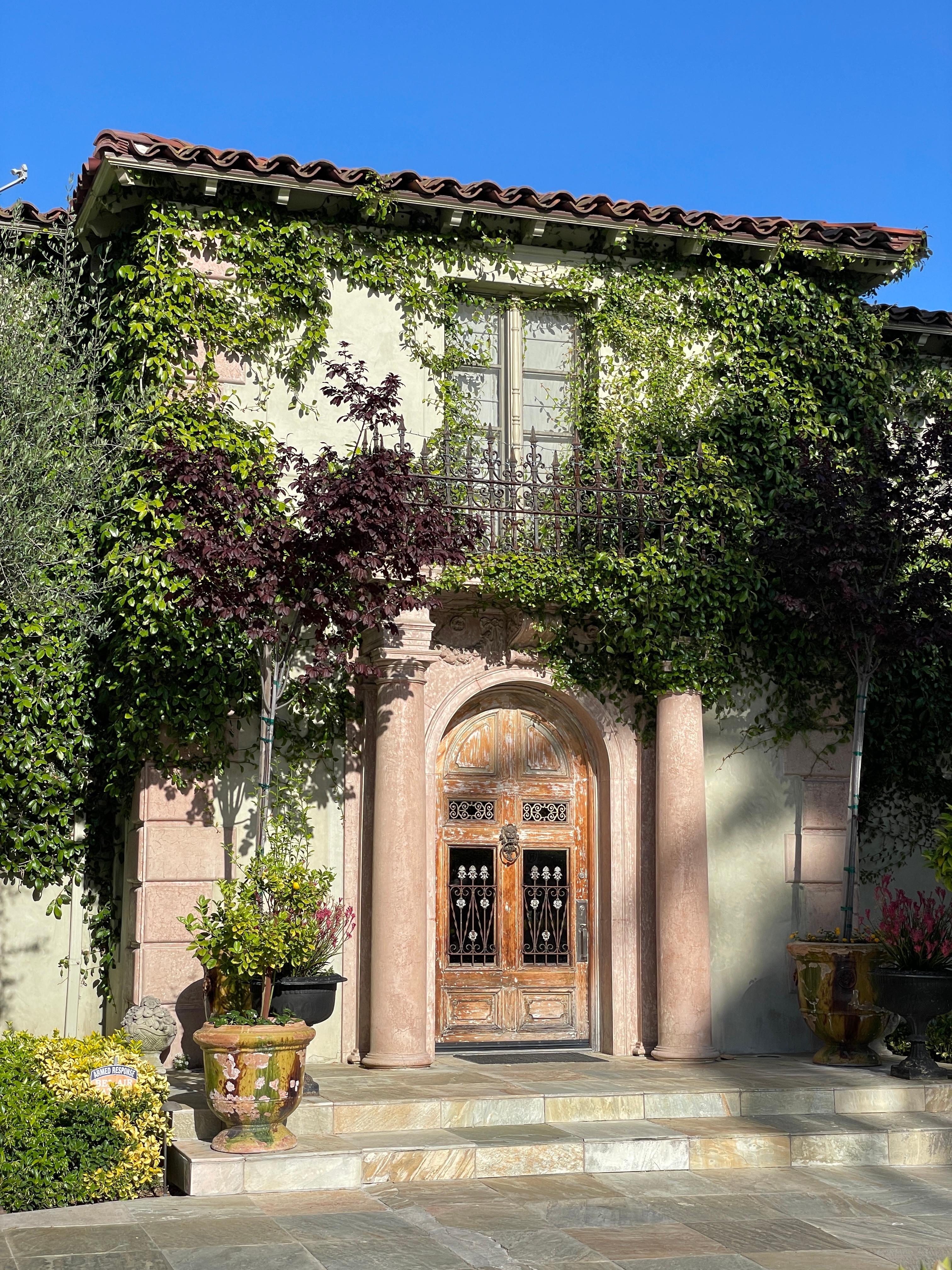 Classic Mediterranean home facade with antique wood doors, well landscaped, and travertine front steps